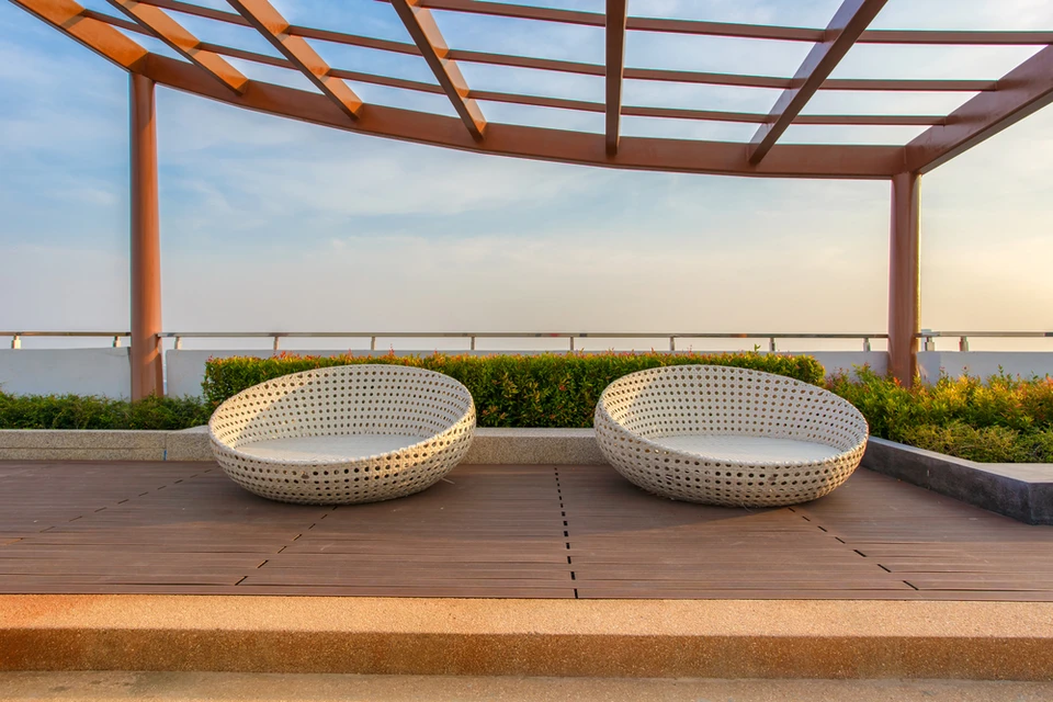 Terrasse extérieure moderne avec deux fauteuils coques en résine tressée beige disposés sur deck en bois exotique