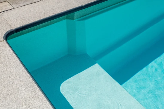 Scène extérieure résidentielle avec piscine creusée ovale à liner bleu, margelles en béton beige
