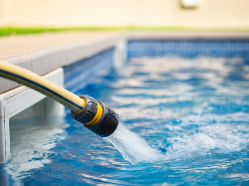Scène extérieure de nettoyage de piscine avec homme utilisant une épuisette à manche télescopique bleu pour nettoyer la surface de l'eau