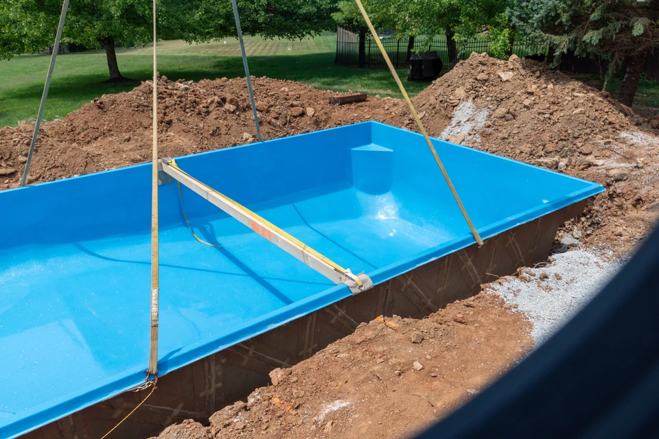 Technicien en combinaison bleue effectuant l'entretien d'une piscine extérieure rectangulaire à eau turquoise, utilisant une épuisette télescopique pour nettoyer la surface