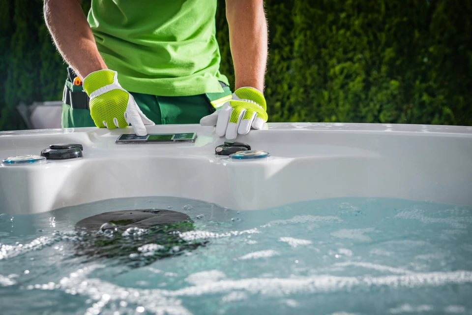 Technicien en position accroupie manipulant un robot nettoyeur de piscine autonome sur margelle en bois
